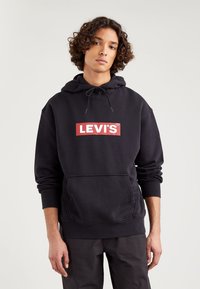 Čierna kapucňová mikina vyrobená z bavlnenej zmesi s červeným obdĺžnikovým logom a bielym textom "LEVI'S" na prednej strane. Klokaní vrecko a rebrované manžety.