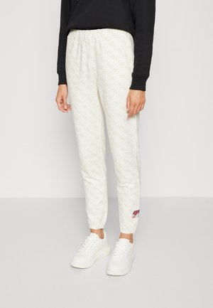 Osoba nosząca białe, wzorzyste spodnie dresowe z elastycznymi ściągaczami i białe trampki, do tego czarną bluzkę z długim rękawem.