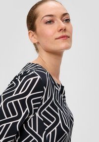 Haut à motif noir et blanc avec un col rond, une coupe près du corps et des lignes géométriques. Le tissu semble lisse avec une légère élasticité.