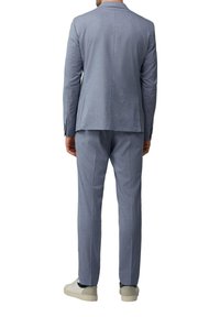 Blau kariertes Anzug mit einer maßgeschneiderten Jacke und passenden Hosen, die eine moderne Passform und strukturierte Stoffe aufweisen. Kombiniert mit weißen Sneakers.