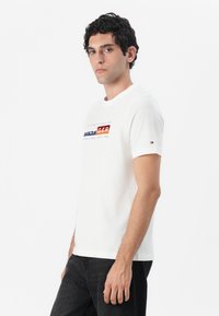White short-sleeve T-shirt featuring a multicolored graphic print across the chest. Cotton material with a crew neck design.