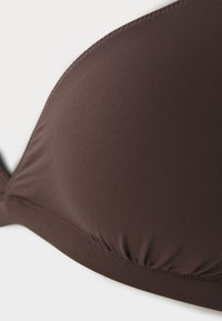 Kafijas krāsas krūšturis ar gludu, elastīgu audumu; ar formas kausu, savāktām detaļām apakšā un tīru, kārtīgu šuvju.