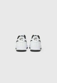 Tênis Nike Air brancos com detalhes pretos, apresentando uma superfície de couro liso, bico arredondado, colarinho acolchoado e sola de borracha texturizada.