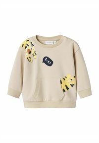 Beige huppari pitkillä hihoilla, etutaskulla ja leikkisillä keltaisilla ja mustilla tiikeriprintillä. Sisältää mustan "RAAR" puhekuplan yksityiskohdan.