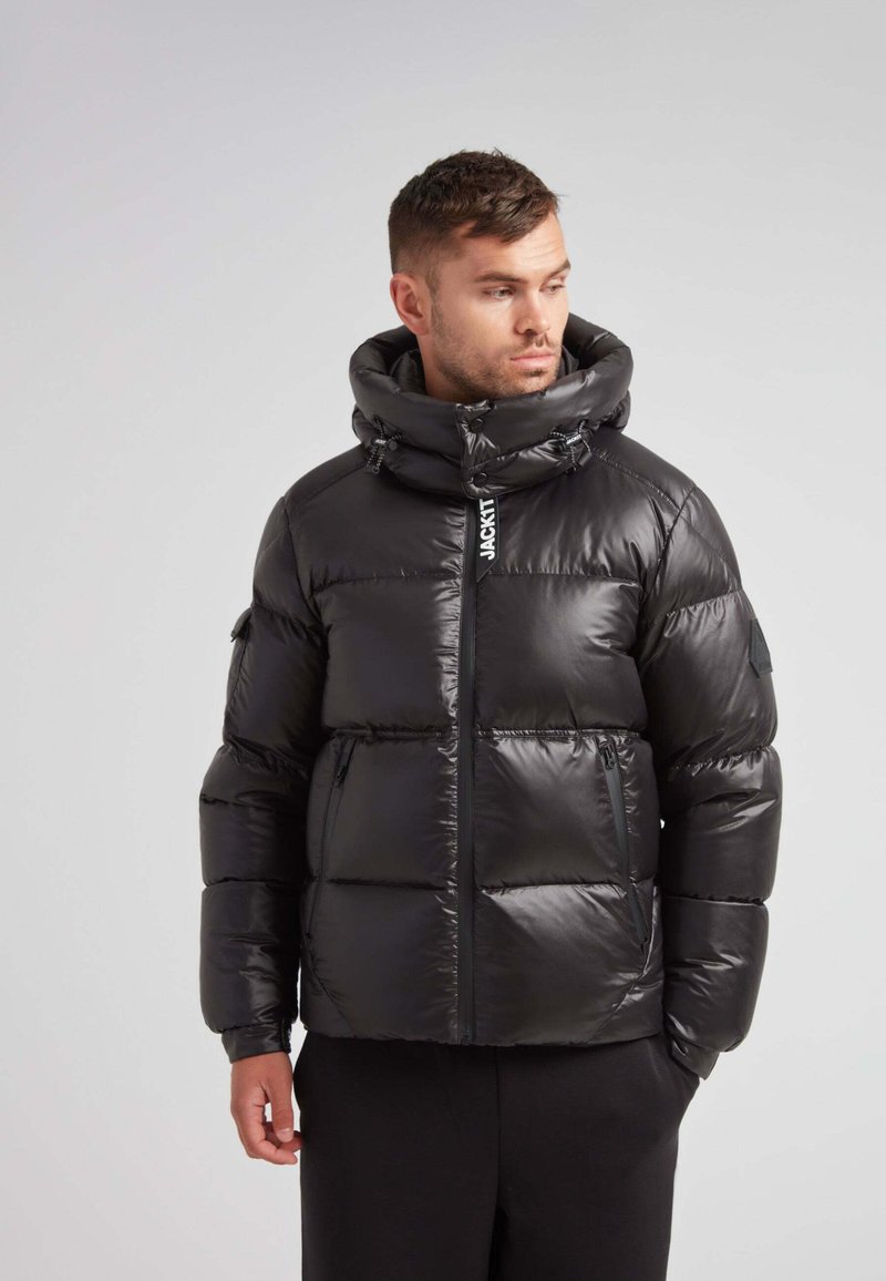 Giacca a vento nera con colletto alto, tasche con zip e texture lucida. Presenta cordini regolabili e un logo sul davanti.