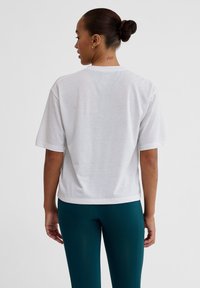 Hvid, kortærmet t-shirt med en afslappet pasform, struktureret stof og rund halsudskæring. Bæres med tætsiddende, teal farvede leggings.