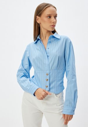 Camisa de botones de color azul claro con rayas verticales, con una cintura ajustada, mangas largas y botones en tono dorado en la parte delantera.