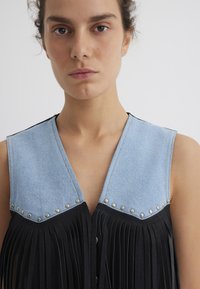 Jeans- und schwarzer Stoffwesten mit metallischen Nieten, einem V-Ausschnitt und fransigen Details an der Vorderseite, die einen Kontrast in der Textur schaffen.
