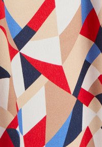 Tissu multicolore présentant des formes géométriques en rouge, bleu, beige et noir. Texture lisse avec un motif subtil et un léger éclat.