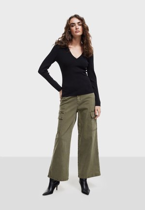 Top negro de manga larga con escote en V combinado con pantalones cargo de pierna ancha en verde oliva. Botines negros de puntera puntiaguda completan el look.