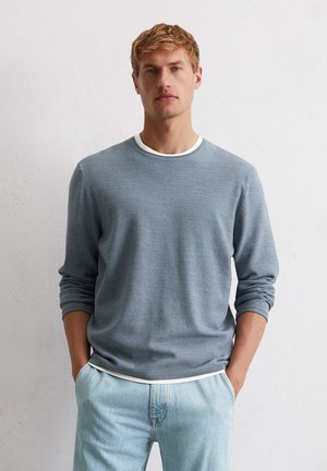 Light blue knit sweater with long sleeves, ribbed cuffs, and a white neckline. Worn over light denim pants, featuring a casual fit.