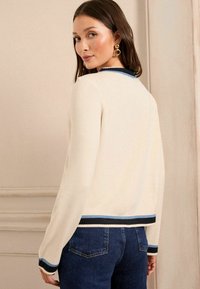 Kermansyen värinen neulepusero, jossa on ribbireunus mustalla ja sinisellä kaula-aukossa ja helmassa. Puserossa on pitkät hihat ja se on slim fit -mallinen.