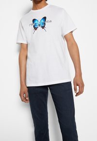 Vitt bomull t-shirt med en blå och svart fjärilsgrafik samt texten "rag & bone NEW YORK", rund hals, korta ärmar och avslappnad passform.