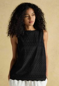 Melna bez piedurknēm blūze ar izšūtām ziedu rotājumiem un viļņotu apakšmalu, izgatavota no vieglas teksturētas auduma.