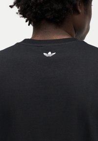 Μαύρο βαμβακερό T-shirt με στρογγυλή λαιμόκοψη και μικρό λευκό λογότυπο στο πίσω μέρος. Λεπτή υφή και απλός σχεδιασμός, εφαρμοστή γραμμή.