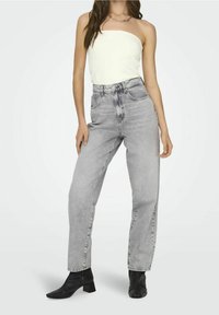 Jeans de cintura alta y pierna recta en denim gris claro con un acabado desvaído. Presenta un diseño de cinco bolsillos y pasadores para cinturón. Llevado con una blusa blanca.