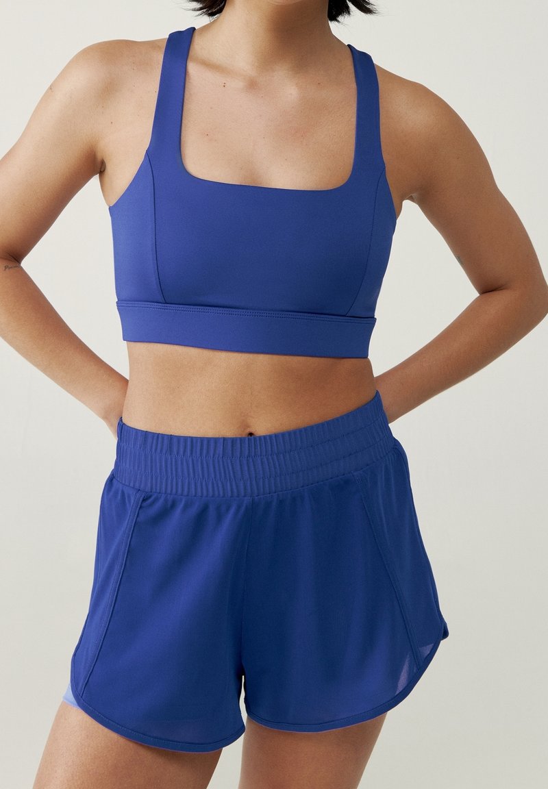 Reggiseno sportivo blu con scollo quadrato e spalline larghe abbinato a pantaloni corti blu larghi con vita elastica e spacchi laterali.
