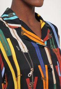 Camicia nera a maniche corte con un motivo a zip colorato a righe, colletto classico e bottoni, realizzata in tessuto leggero.