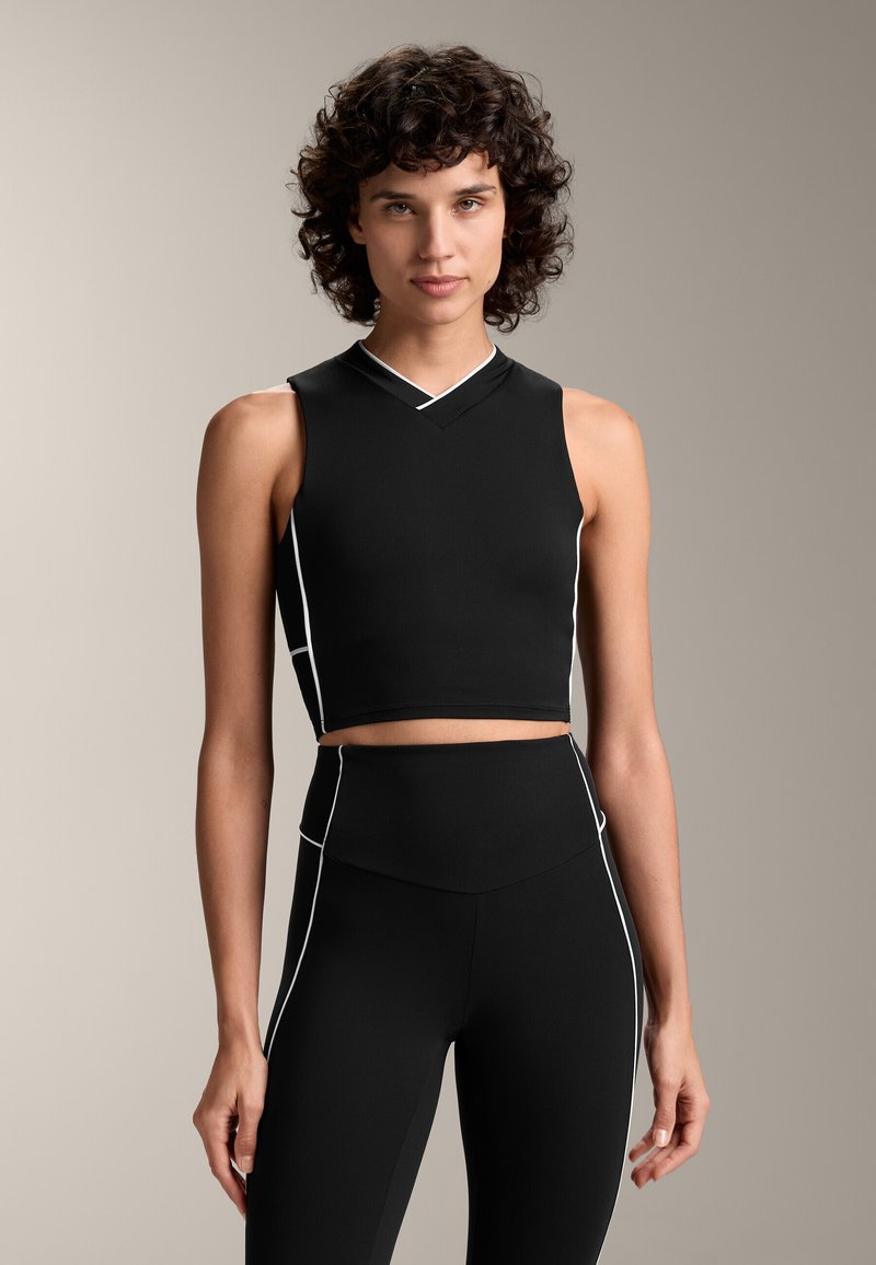 Mustat lyhyet topit, joissa on tiukka muotoilu, valkoisella kontrastitikkauksella ja V-pääntiellä. Sileä, joustava kangas ilman hihoja.