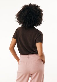 Bruine short-sleeve top gecombineerd met lichtroze op maat gemaakte broeken. De stof heeft een gladde textuur, met subtiele ontwerpelementen aan de achterkant.