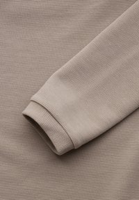 Kangasta beige, ribbimäisellä pinnalla ja taitetulla hihalla. Pintakuvio on tekstuuri, ja muotoilu on yksinkertainen ja hyödyllinen, sopii arkivaatteisiin.