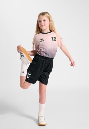 Junges Mädchen in Sportbekleidung, das ein Bein nach hinten streckt und den Fuß hält, steht auf einem Bein vor einem einfarbigen Hintergrund.