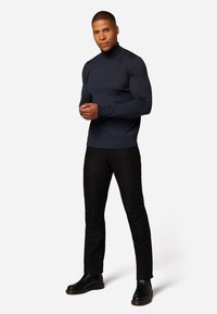 Marineblauwe coltrui met een aansluitend ontwerp en lange mouwen, gecombineerd met zwarte broek en zwarte enkellaarsjes met een textuurzool.