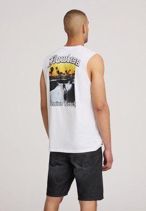 T-shirt bianca senza maniche con una grafica di un skatepark, palme e il testo "Flawless Venice Beach" in tonalità di nero e giallo.