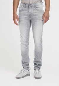 Jeans en denim gris clair à coupe slim, légère décoloration, cinq poches et braguette à glissière. Associés à des chaussures de sport gris clair.