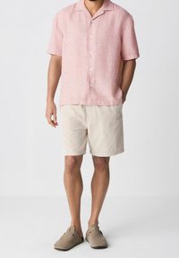 Camisa de manga corta de color rosa con estampado, pantalones cortos beige y zapatos de lona color camello. La camisa tiene un diseño abotonado y un corte relajado.