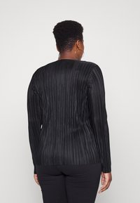 Top lungo nero a maniche lunghe con texture a righe verticali e scollo rotondo. Il tessuto ha una finitura liscia che esalta la silhouette.