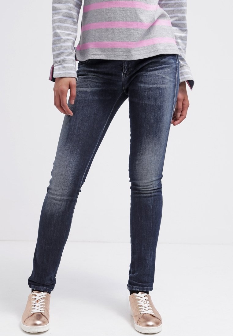 Jean skinny en denim bleu foncé avec légères décolorations, associé à un haut à manches longues rayé gris et rose, et des baskets métalliques rose doré.