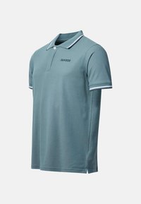 Polo manches courtes couleur sarcelle avec col et poignets rayés blancs, patte de boutonnage et texte "SEASIDE" sur la poitrine.