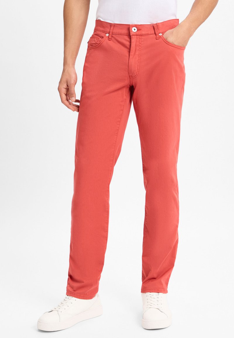 Rote Baumwollmischung-Hosenträger mit geradem Schnitt, Fünf-Taschen-Design, Metallknopfverschluss und dezenter Textur. Getragen mit weißen Turnschuhen.