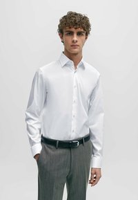 Chemise blanche à manches longues avec un col formel et un devant boutonné, accompagnée d'un pantalon gris à rayures et d'une ceinture noire. Texture lisse.