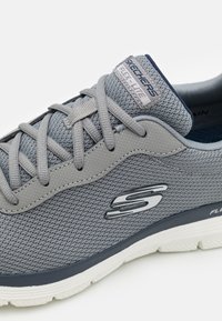 Grey athletic shoe with breathable mesh upper, laces, and padded collar. Features a flexible, white outsole and logo on the side.