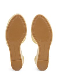 Paire de chaussures compensées beige vues de la semelle, avec des semelles en caoutchouc texturées et le logo "Tommy Hilfiger" sur chaque semelle.