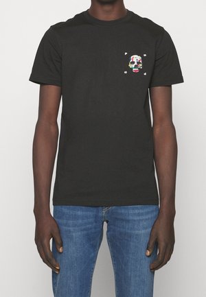 Sort kortærmet t-shirt med farverigt kranie-grafik og bogstaverne "P", "S", "D" omkring det, båret af en person i blå jeans.