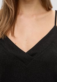 Vêtement noir avec un design à col en V et de fines bretelles. Le tissu a une texture subtile et des détails scintillants, mettant en valeur son apparence élégante.