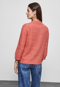 Maglione rosso con texture, maniche a tre quarti, colletto rotondo e vestibilità rilassata, abbinato a pantaloni in denim blu.