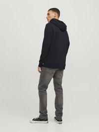 Felpa nera con cappuccio dal taglio comodo, abbinata a jeans grigi. L'outfit è completato da sneakers basse bianche e nere.