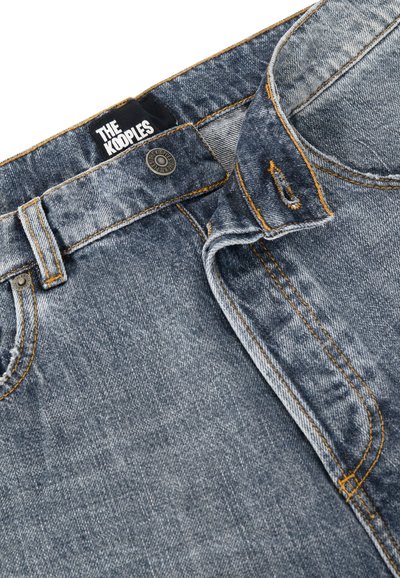 Jeans de mezclilla en azul desgastado con costuras naranjas, con cierre de botón y presillas para cinturón. La etiqueta dice "THE KOOPLES". La textura es suave y usada.