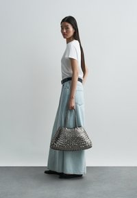 Geweven metallic grijze handtas met dubbele handvatten, gecombineerd met een wit T-shirt en een lichtblauwe denim rok. Soepele texturen en casual ontwerp.