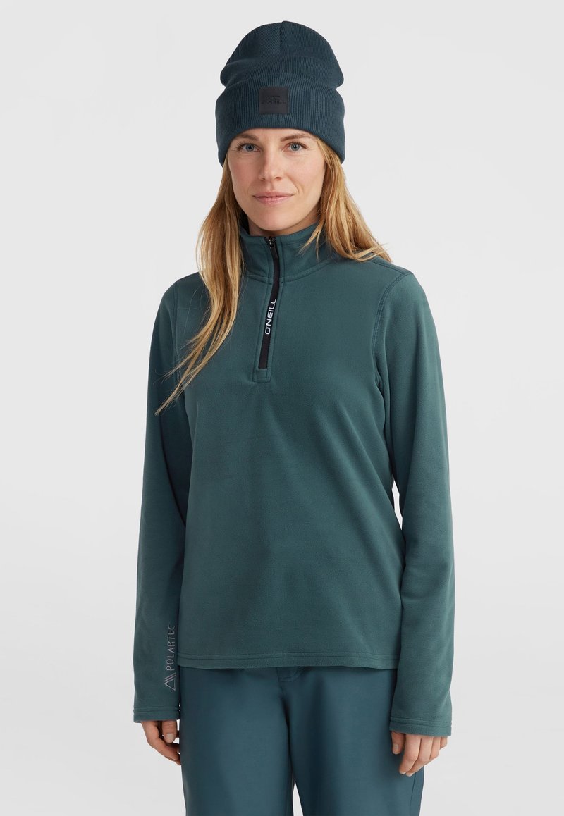 Tmavě modrý fleece pulovr s čtvrtinovým zipem, vyzývavý s logem na zipu a rukávu. V kombinaci s odpovídajícími tmavě modrými kalhotami.