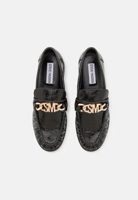 Mustad musta nahast loafers, millel on krokodillikujuline tekstuur, kullast detailid ja pehme krae. Omab logot rihmal ja siledat sisemust.