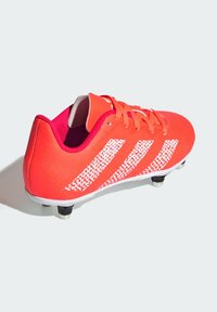 Puntti jalkapallokengät, joissa on teksturoitu pinta, valkoiset raidat ja oranssit nauhat. Varustettu muotoillulla pohjalla, jossa on mustat nupit pitävää otetta nurmipinnoilla.