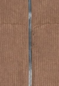 Gros plan sur un tissu en velours côtelé marron avec une fermeture éclair en métal argenté centrée.