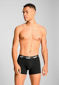 Black cotton boxer briefs with a wide elastic waistband featuring a white logo. The design is form-fitting and mid-thigh length.