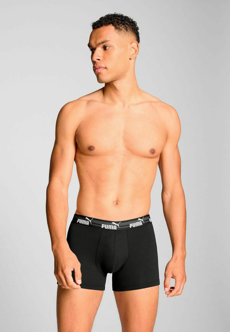 Black cotton boxer briefs with a wide elastic waistband featuring a white logo. The design is form-fitting and mid-thigh length.