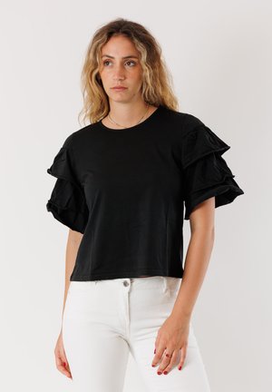 Top nero a maniche corte con maniche arricciate, scollatura rotonda e vestibilità morbida. Indossato con pantaloni bianchi, che dimostrano uno stile casual.